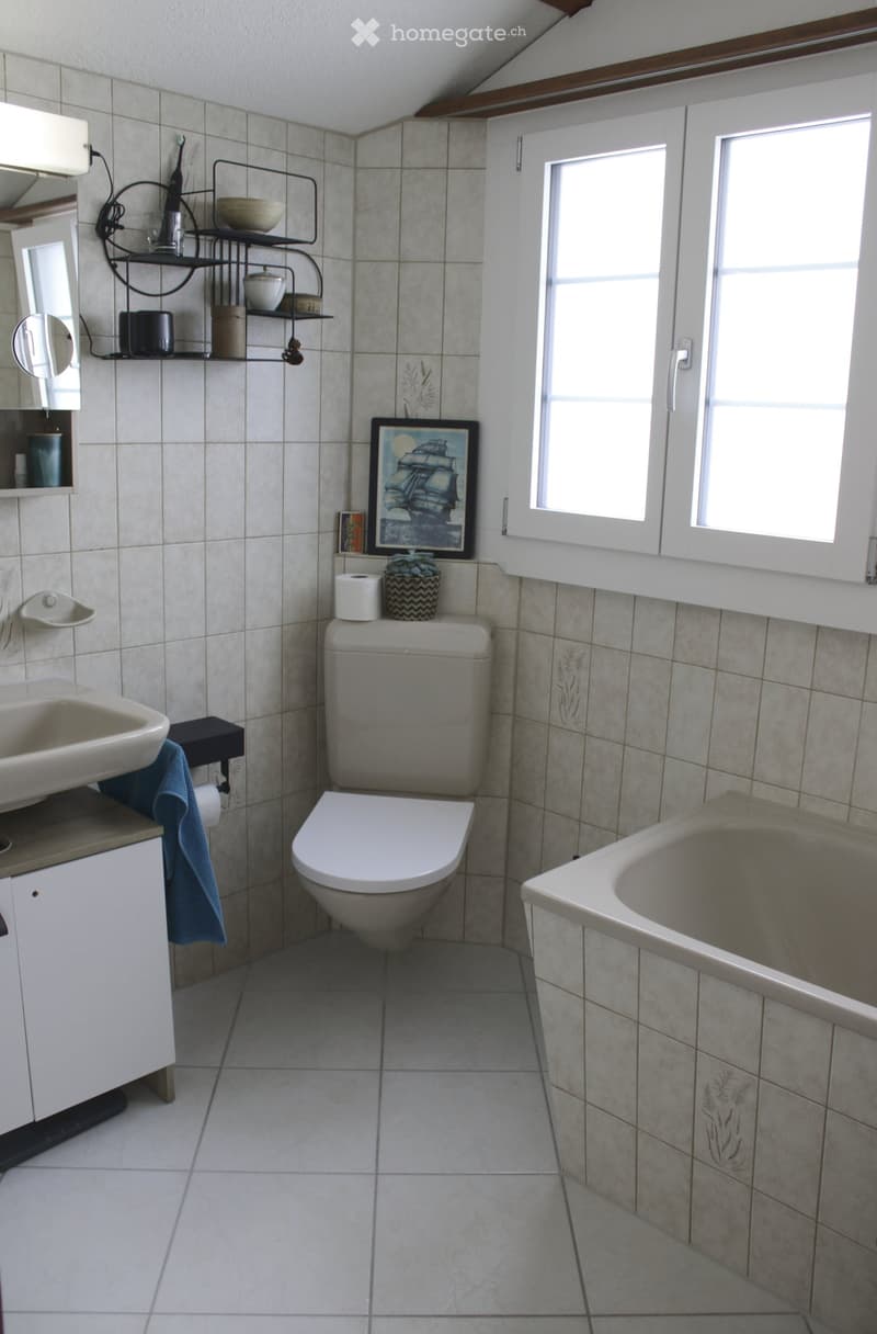Bathroom with a toilet, sink, bathtub, mirror, and cabinet. Includes a towel, picture frame, and shelf with various items.