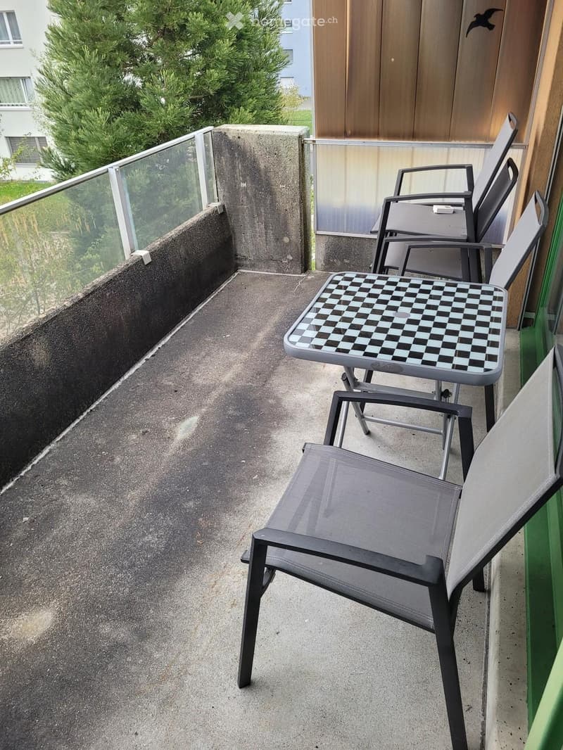 Balcony with a concrete floor, glass railing, and outdoor furniture including a table and chairs.