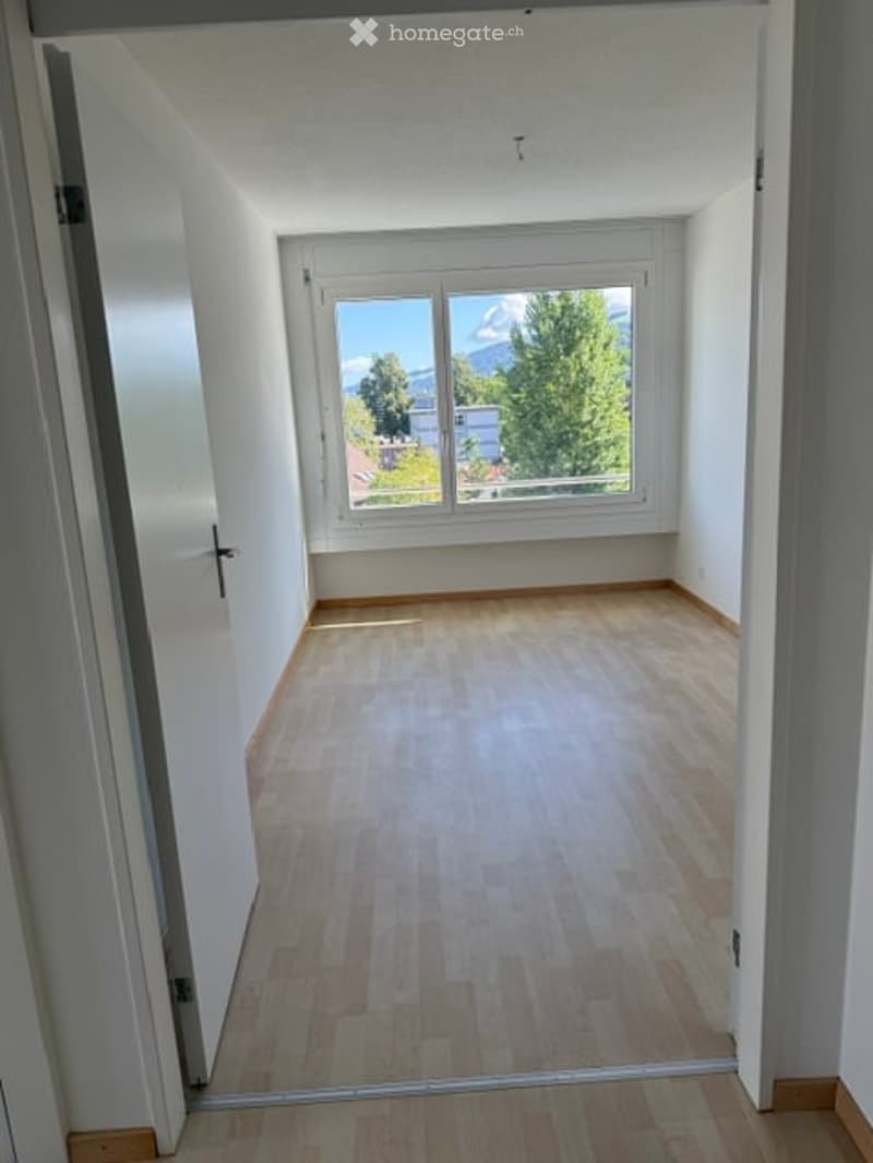 Empty room with wooden flooring, large window offering a scenic view, and white walls.