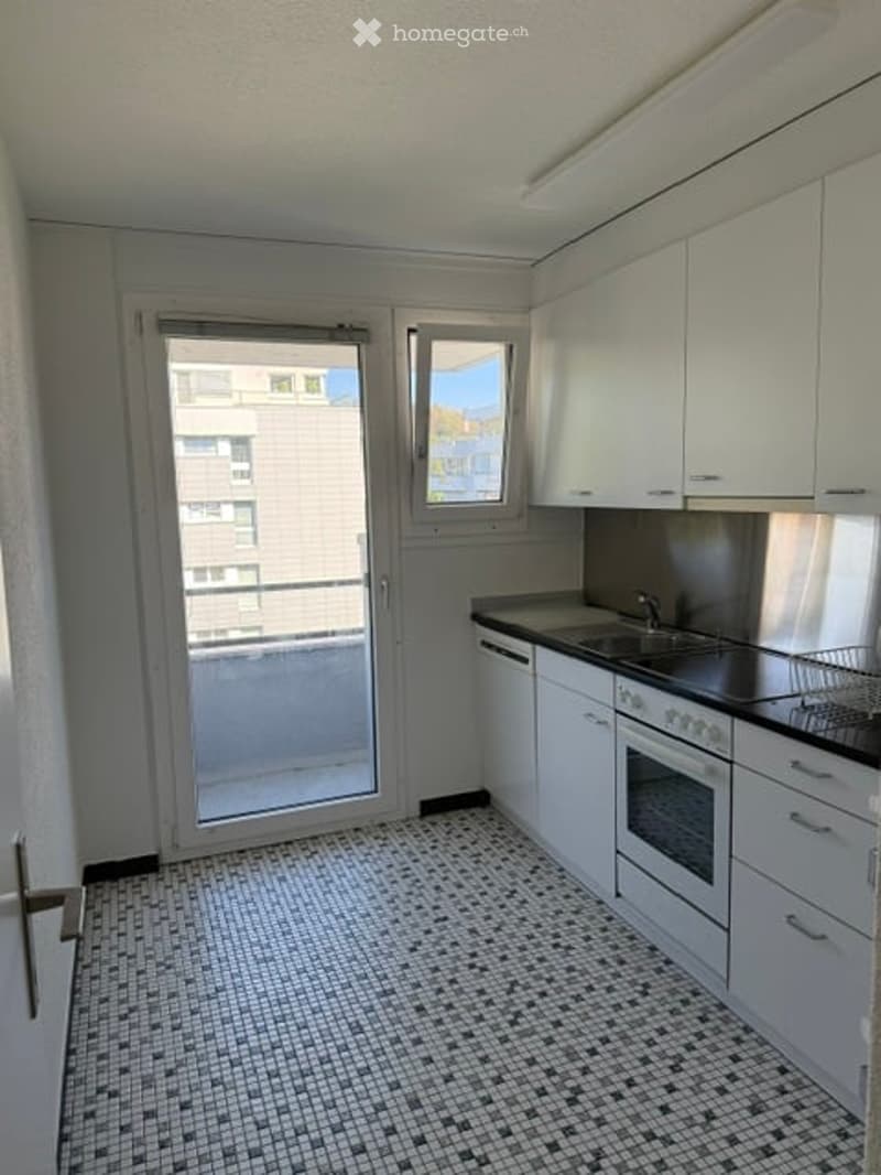 Modern kitchen with white cabinets, black countertops, and a tiled floor. Features a sink, oven, and a window with a view of a building.