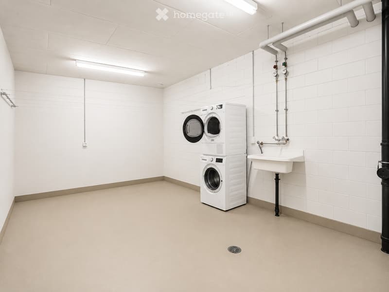 Clean, modern laundry room with white tiled walls, a stacked washer and dryer unit, and a white sink with a faucet.