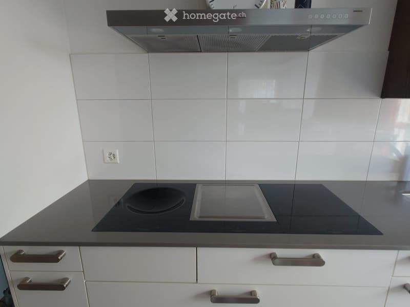 Modern kitchen with white tiled walls, black countertop, induction cooktop, and stainless steel range hood.