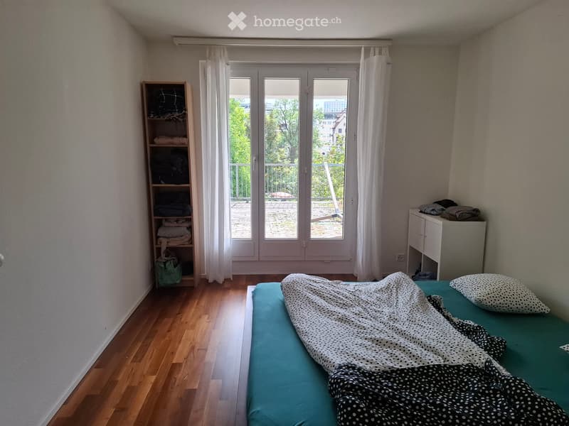 Bedroom with wooden floor, bed with blue mattress and black and white polka dot blanket, pillow, wardrobe, shelf, and balcony access.
