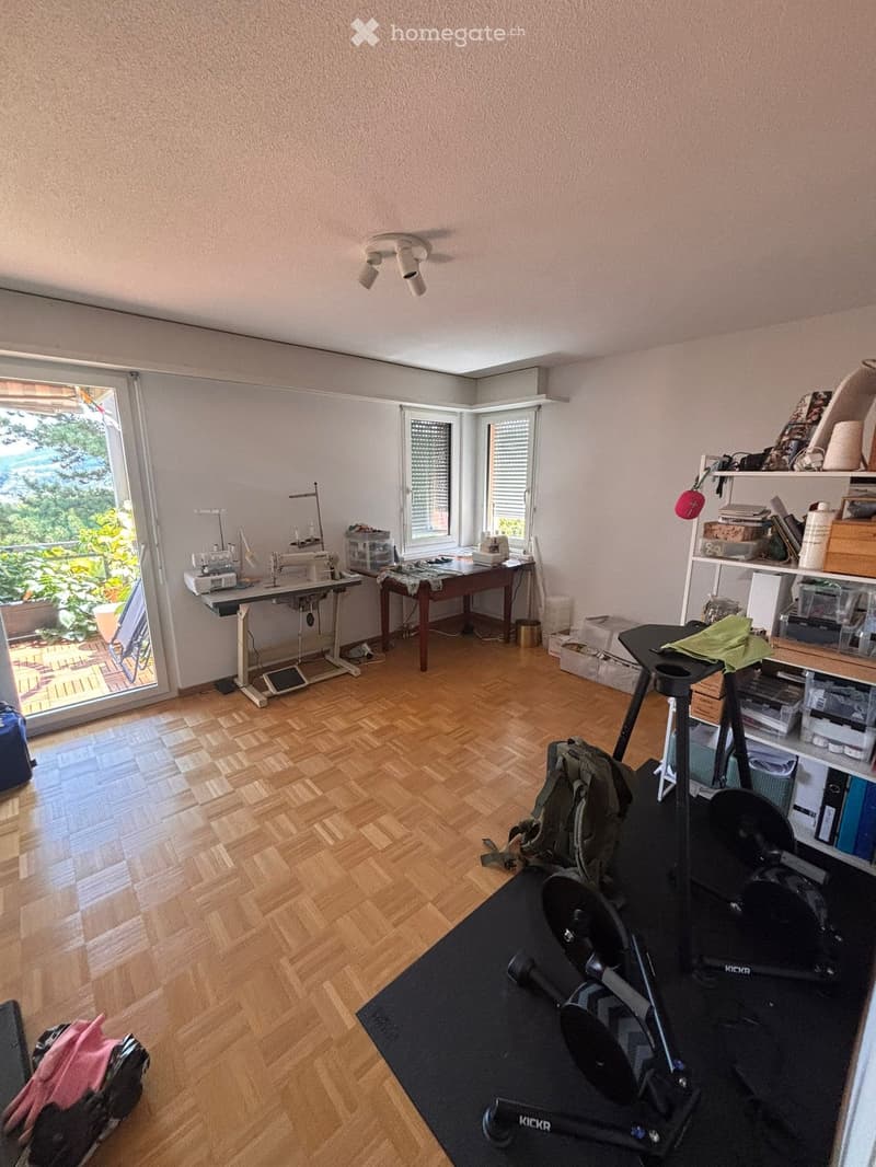 Well-lit room with wooden flooring, large windows, sewing machine, shelves, and exercise equipment.