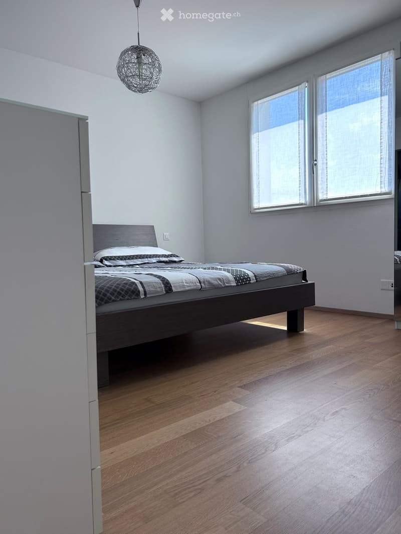Modern bedroom with wooden flooring, a dark wooden bed with a grey and black checkered duvet, and a hanging spherical light fixture.
