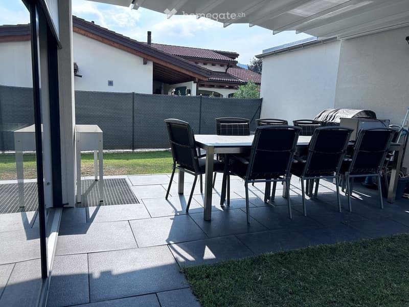 Outdoor patio with tiled floor, dining table and chairs, covered area, and view of neighboring house and garden.