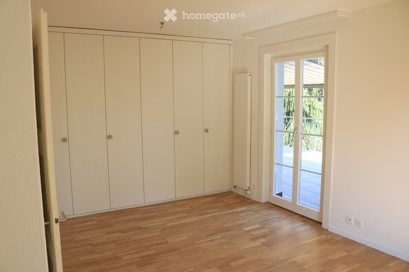 Empty room with light wooden flooring, white walls, large built-in wardrobe, and a sliding glass door leading to a balcony or outdoor area.