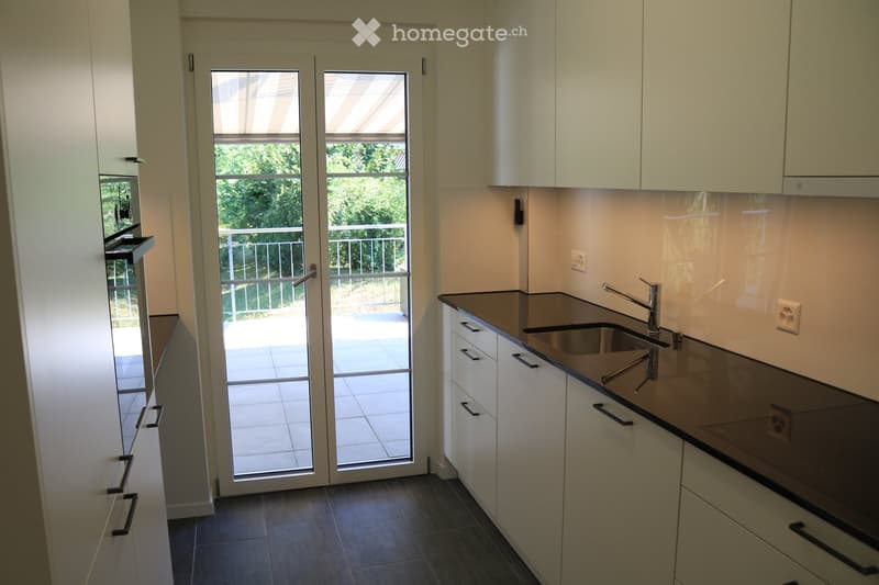 Modern kitchen with white cabinets, dark countertops, a sink with a faucet, and an oven. Features a large glass door leading to a balcony.