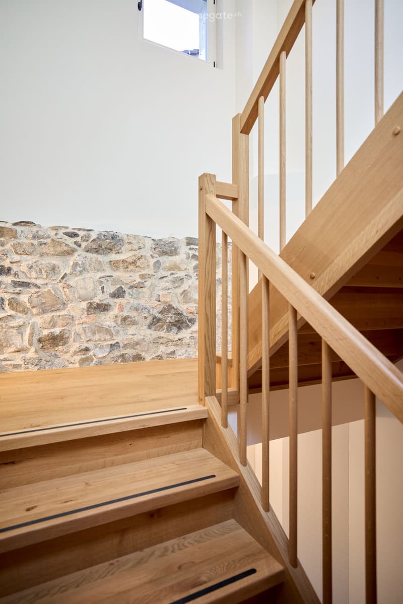 Wooden staircase with a light wooden railing and a stone wall in the background.