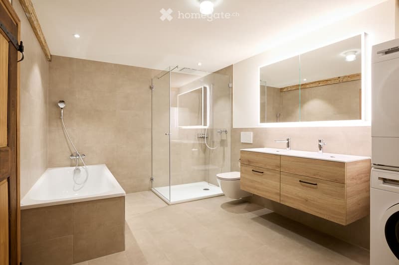 Modern bathroom with a bathtub, separate shower, toilet, sink, and wooden cabinet. Features a large mirror and sleek fixtures.