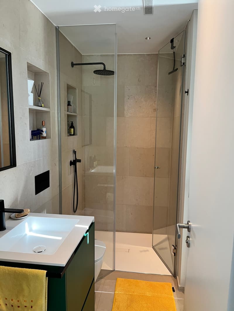 Modern bathroom with a white sink, black faucet, glass-enclosed shower, and a yellow bath mat.