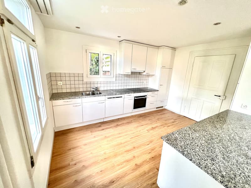 Modern kitchen with white cabinets, granite countertops, wooden flooring, and built-in appliances including a sink, oven, and dishwasher.