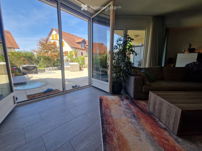 Bright living room with large sliding glass doors opening to a patio, featuring a sofa, coffee table, and a colorful rug.