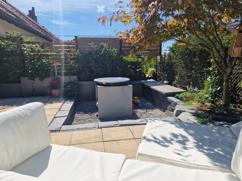 Garden with a modern seating area, stone pathways, a small water feature, and various plants and trees.