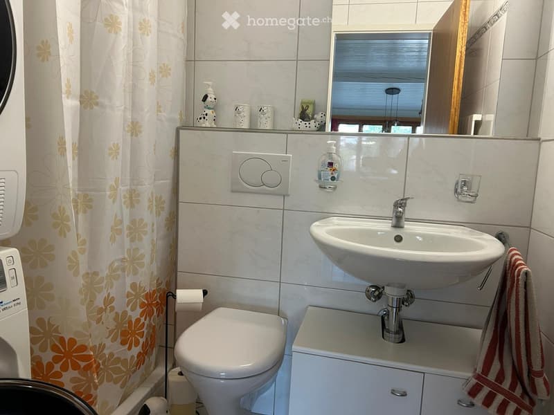 Modern bathroom with white tiles, a toilet, a sink with a mirror, a towel, and a shower curtain with a floral pattern.