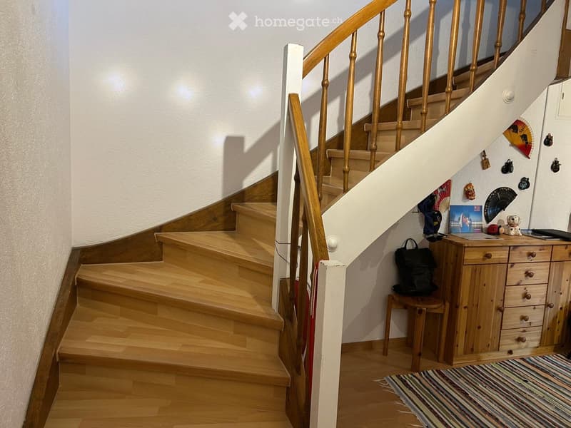 Wooden staircase with handrail, small wooden cabinet with drawers, stool, backpack, fan, picture frame, and laptop on the landing.