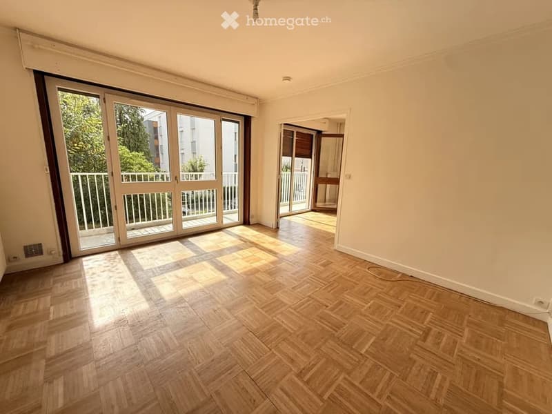Empty room with wooden flooring, large sliding glass doors leading to a balcony, and natural light streaming in.