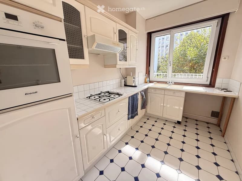A modern kitchen with white cabinets, a gas stove, an oven, a sink, and a dishwasher. The floor features a white and blue hexagonal tile pattern.
