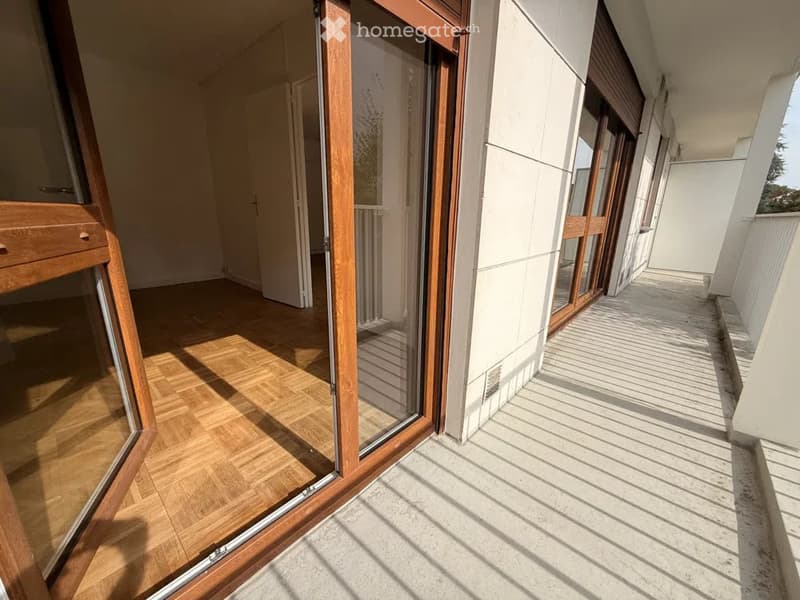 Balcony with wooden flooring and glass sliding doors, leading to a hallway with wooden flooring and white walls.