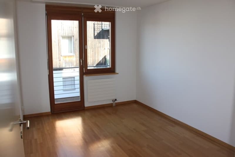 Empty room with wooden flooring, white walls, and a large window with a sliding door leading outside.