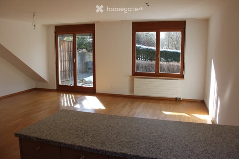 Empty room with wooden flooring, large windows, sliding glass doors, and a granite countertop with cabinets.