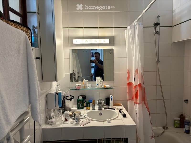 Bathroom with a sink, mirror, cabinet, towel, shower curtain, and various toiletries on the counter.