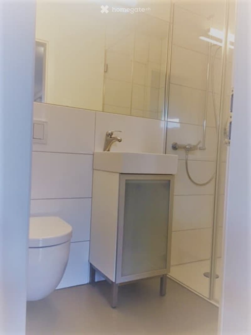 Modern bathroom with white tiles, a toilet, a sink with a faucet, and a glass-enclosed shower area.