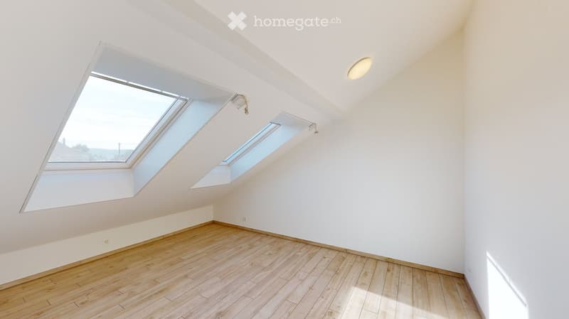 Bright, empty attic room with wooden flooring, white walls, and large skylight windows allowing natural light to fill the space.