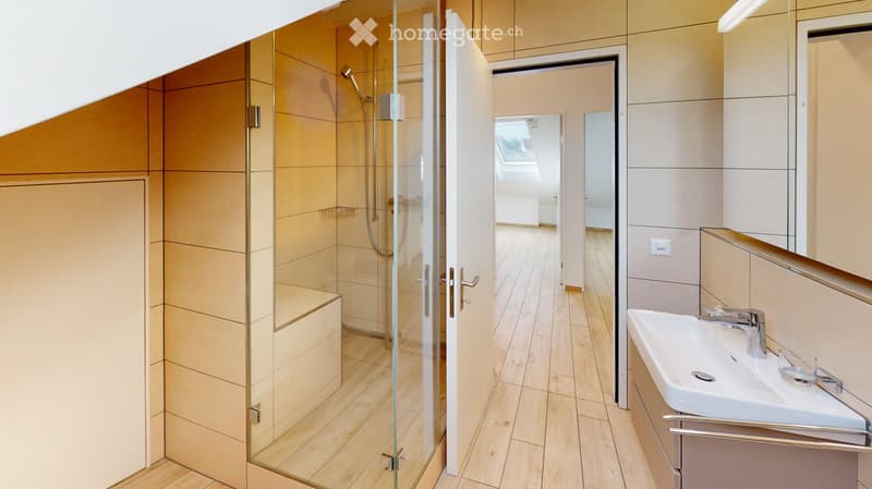 Modern bathroom with a glass-enclosed shower, a white sink with a chrome faucet, and light wooden flooring.