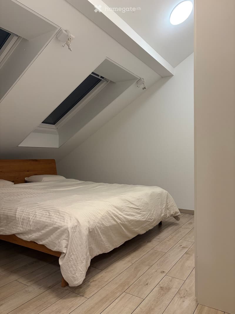 Cozy attic bedroom with wooden flooring, a single bed with white bedding, and a skylight window above the bed.