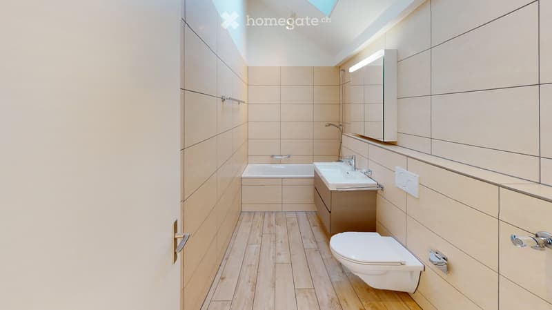 Modern bathroom with light-colored tiles, wooden flooring, a bathtub, sink, toilet, and a mirrored cabinet.