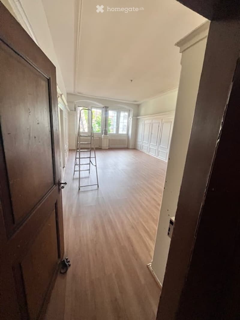 Empty room, wood floor, ladder in the corner, white walls, windows, radiators