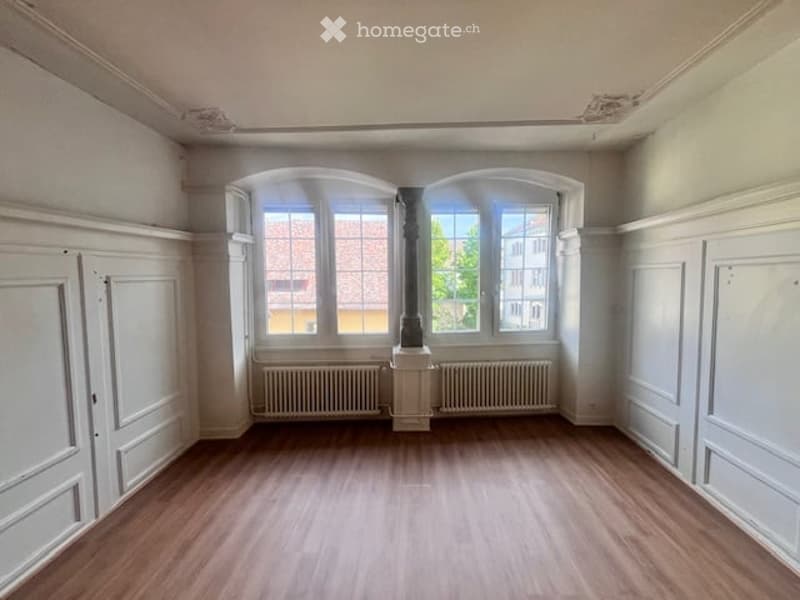 empty room with white walls, wooden floor, two arched windows, white doors, white trims, white radiators