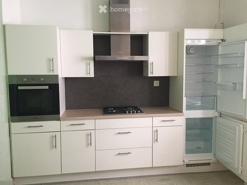 a clean and empty kitchen with all white cabinets, countertops, an oven, a stove, and an open refrigerator