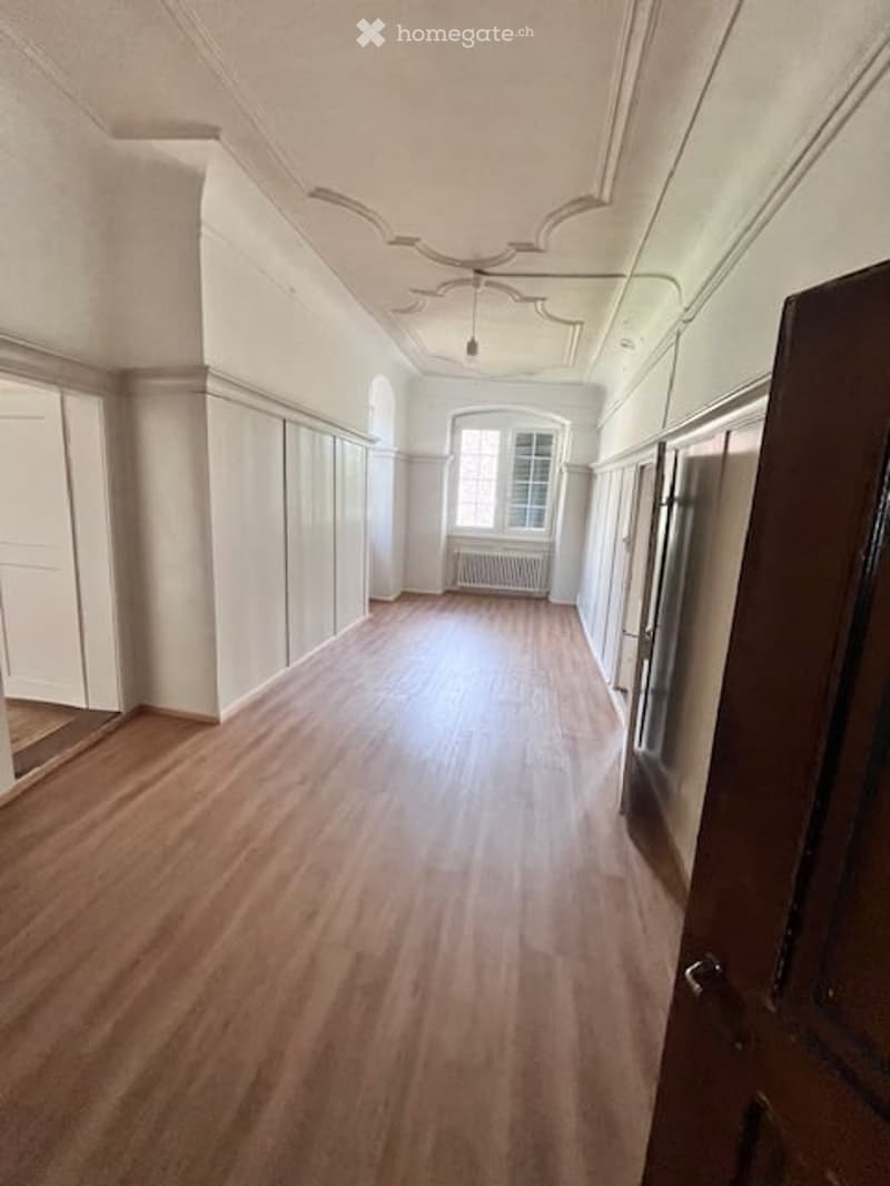 empty room, wooden floor, white walls, large window with white curtains, radiator, corridor with doors