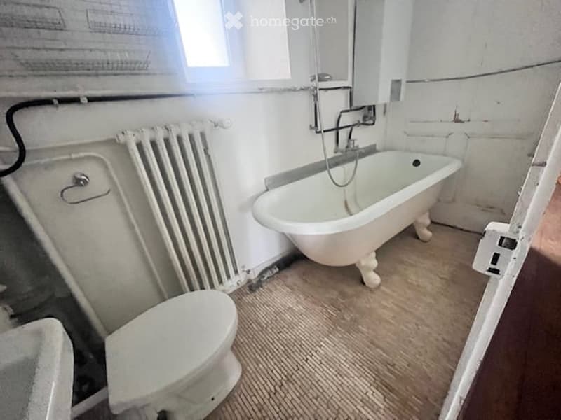 Bathroom with a bathtub, toilet, sink, radiator, and an electrical outlet.