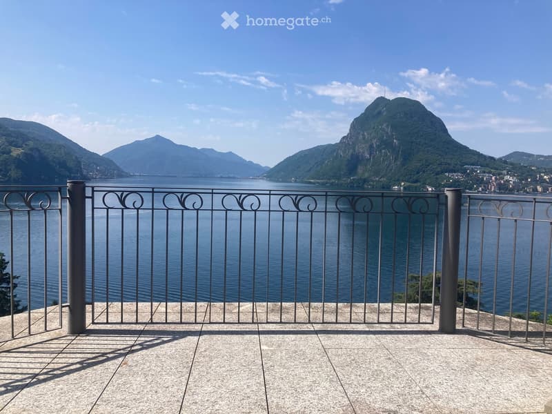 Balcony overlooking a lake with a scenic mountain backdrop, featuring a metal railing and tiled floor.