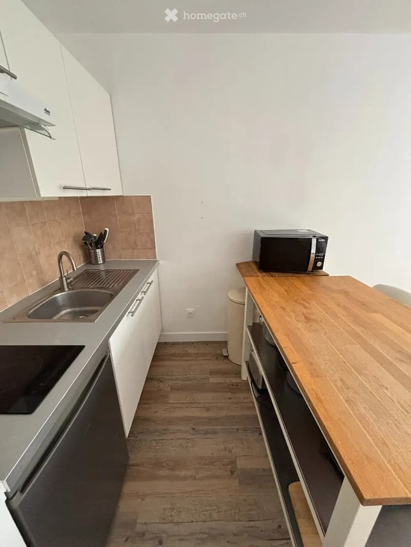 Modern kitchen with white cabinets, wooden table, microwave, sink, and oven.