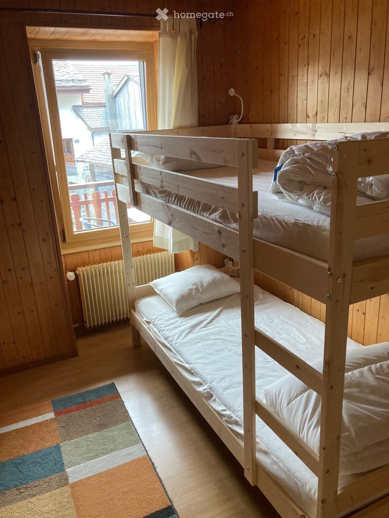 Cozy wooden bedroom with bunk beds, white bedding, a radiator, and a window with a view of the roof.