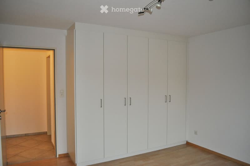 Empty room with white built-in wardrobes, wooden flooring, and a doorway leading to another space.
