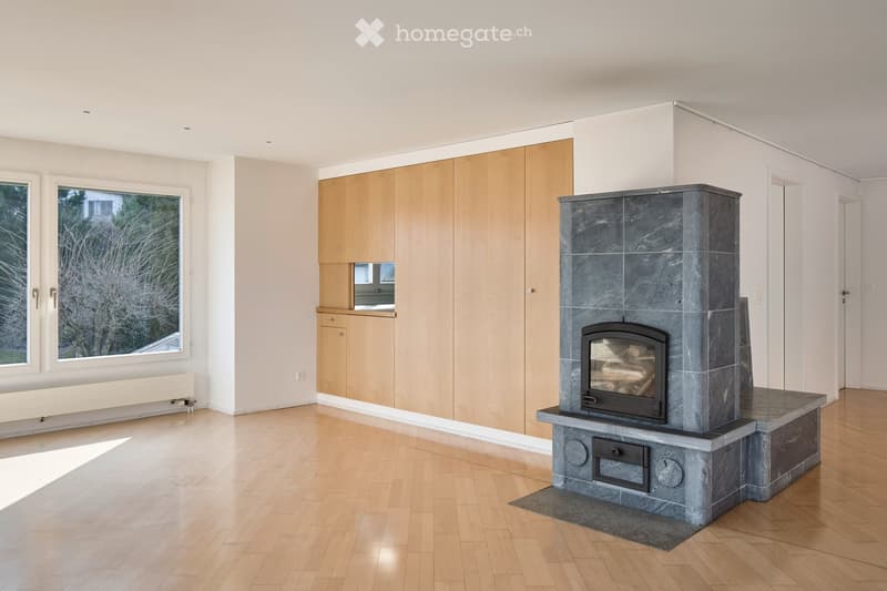Modern living room with light wooden flooring, large windows, and a stone fireplace.