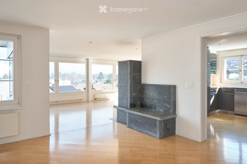 Bright, open living space with wooden flooring, large windows offering a view, and a stone fireplace. The room is empty, with no furniture or furnishings visible.