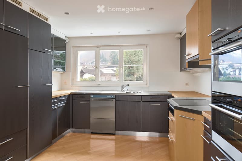Modern kitchen with dark wood cabinets, stainless steel appliances, and a light wooden floor. Features a sink, faucet, dishwasher, and oven.