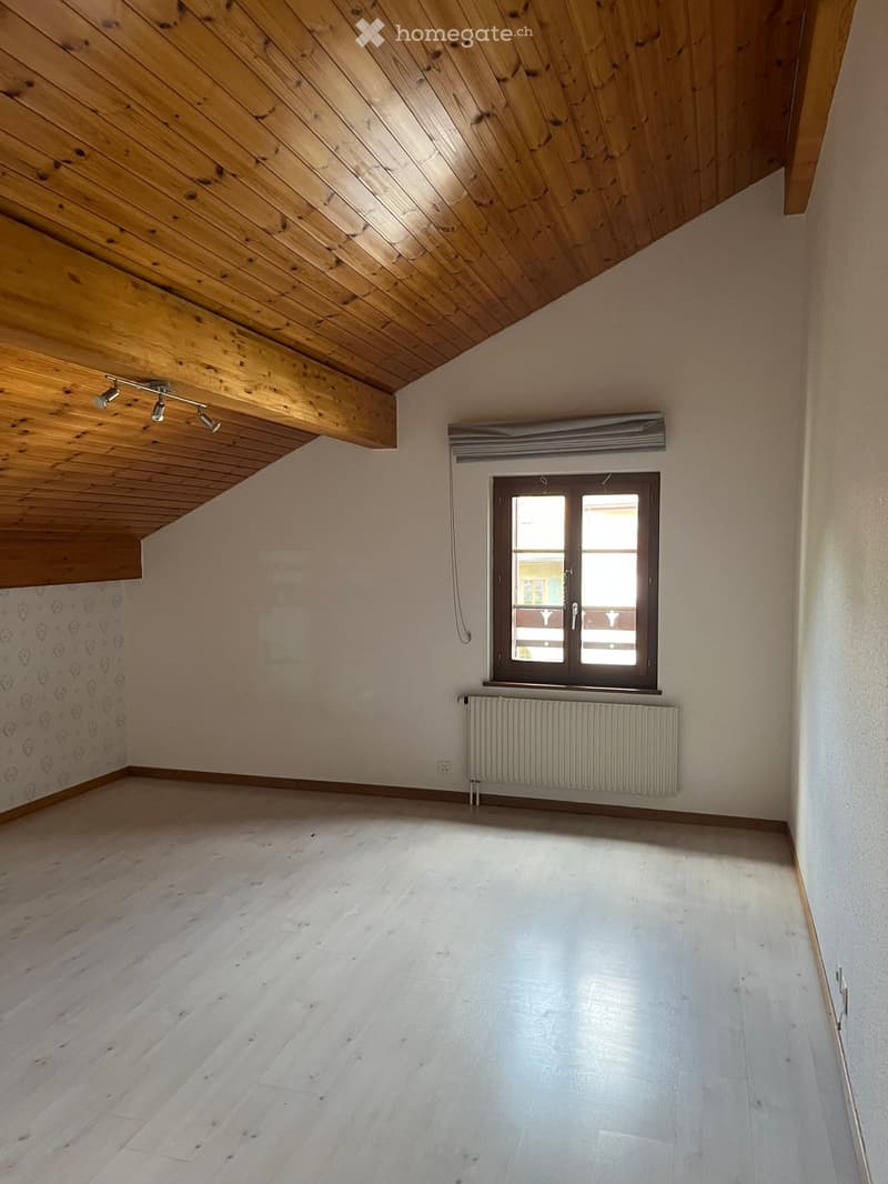 Empty room with wooden ceiling, light wooden floor, window with blinds, radiator, and decorative wall pattern.