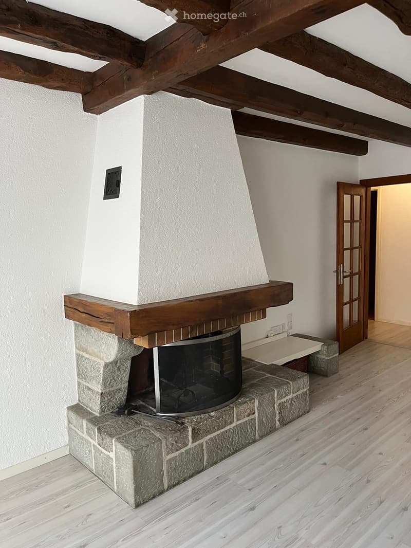 Room with exposed wooden beams, a stone fireplace with a wooden mantel, and a wooden floor.