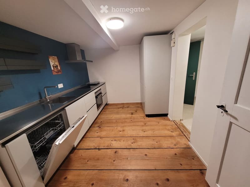 Modern kitchen with wooden flooring, white cabinets, stainless steel sink, dishwasher, oven, and refrigerator. Blue accent wall with a decorative poster.