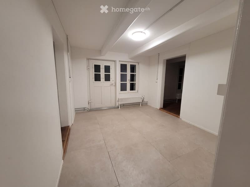 Empty hallway with tiled floor, white walls, a door with glass panels, and a radiator.