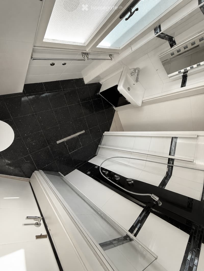 Modern bathroom with black tiled floor, white walls, a sink, bathtub, and a large mirror. Features a sleek, contemporary design with glass elements and built-in storage.
