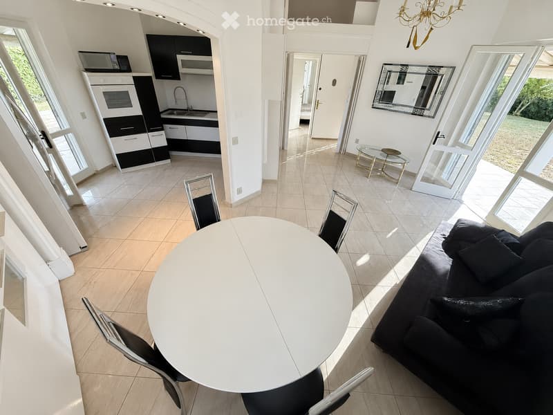 Modern living and dining area with large windows, a black sofa, a white dining table with chairs, a coffee table, and a mirror on the wall.