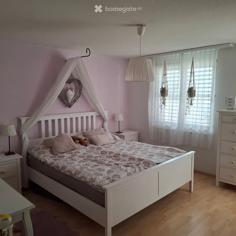 A cozy bedroom with a white bed, floral bedding, nightstands, lamps, and a decorative heart-shaped wall hanging.